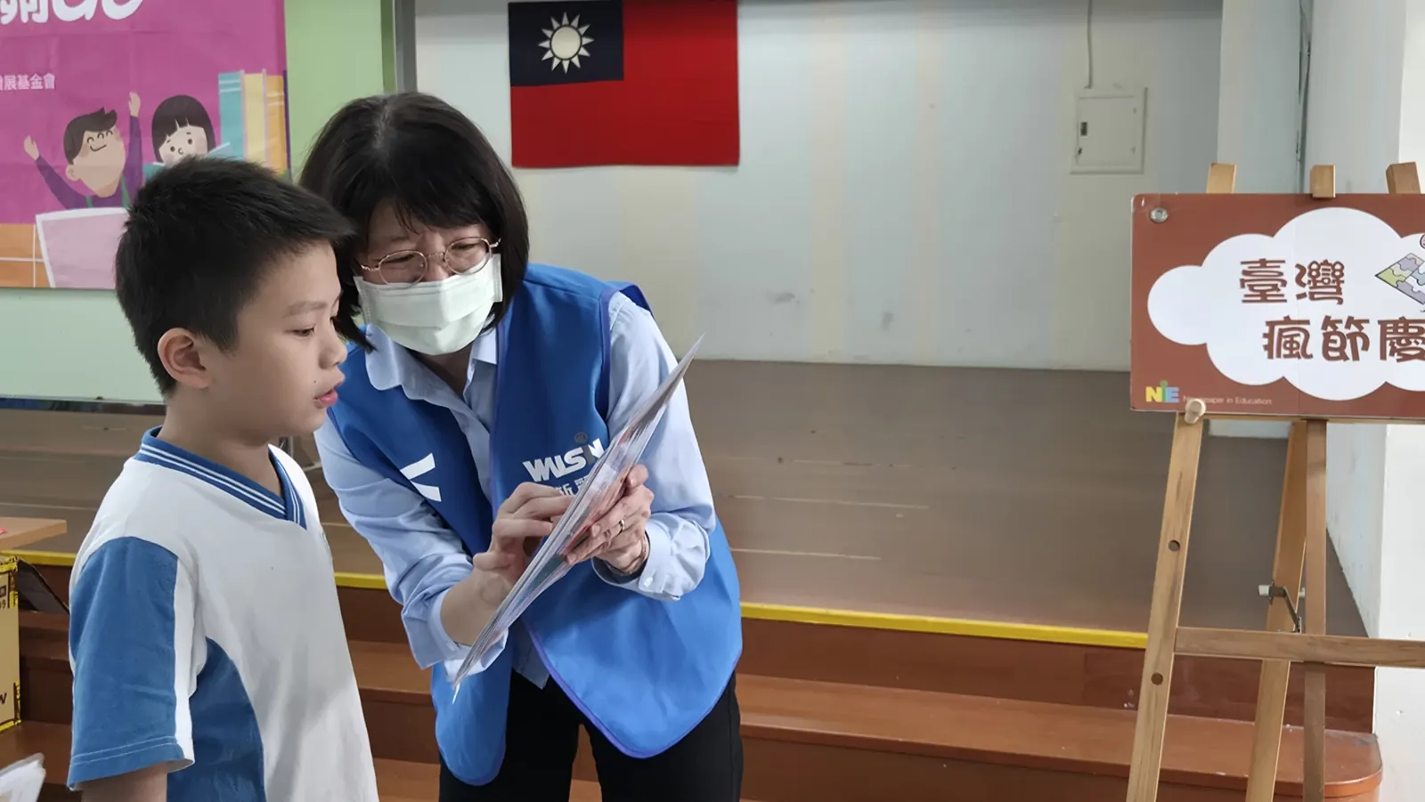志工彎腰陪學童看題卡，閱讀教育推廣活動